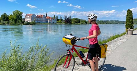 Frau mit Rad steht an der Donau und sieht in die Ferne 