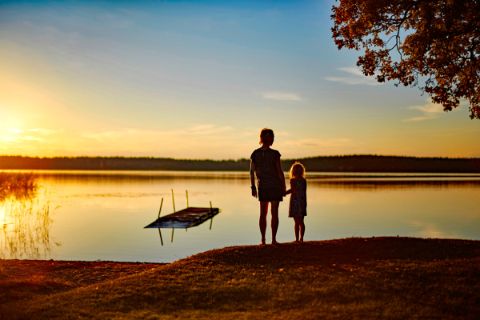 Mutter mit Tochter Hand in Hand im Abendrot am See in Schweden