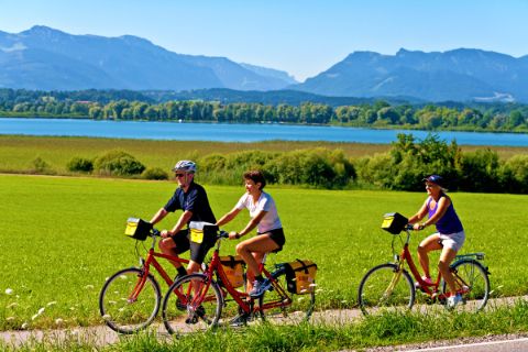 Drei Radfahrer mit Chiemsee und den bayerischen Alpen im Hintergrund