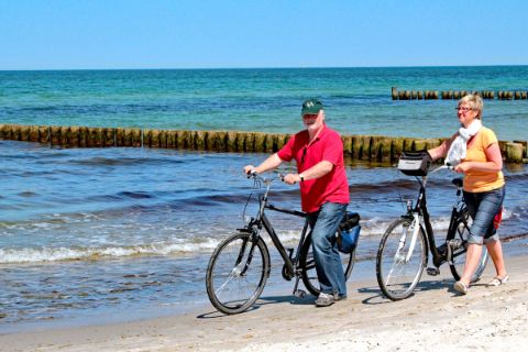 Radfahrer die ihr Rad am Strand entlang schieben in Nordfriesland