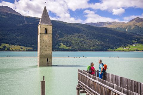 Hikers admire the mystical Reschensee lake with its sunken church tower