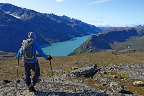 Hiker enjoys the view of large mountain lake and mountains in Jotunheimen National Park