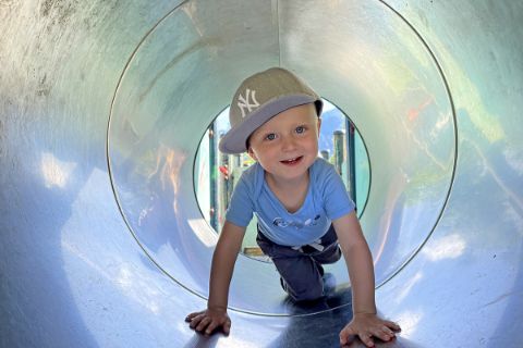 Kind krabbelt durch eine Röhre am Spielplatz in Bad Goisern