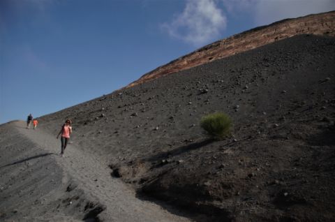 Mehrere Wanderer wandern auf einem schmalen Pfad den Vulkan hoch.