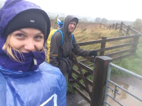 2 Wanderer stehen an einem Zaun und sind vom Regen ziemlich nass.