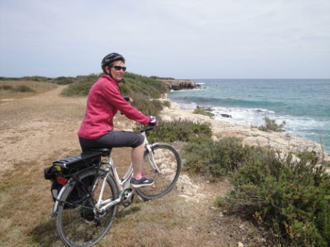 Velofahrerin steht an einer Klippe und betrachtet das Meer. Sizilien Südost. Veloferien mit Eurotrek. 