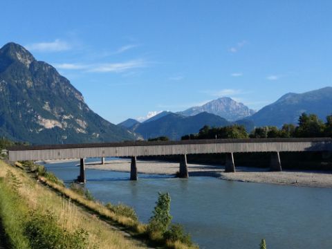 Un pont en bois enjambe une rivière avec des montagnes en arrière-plan. 