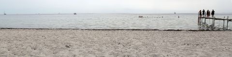 Ein paar Leute stehen auf einem Steg der vom Sandstrand ins Meer führt.