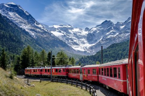 Die Rhätische Bahn fährt auf dem Bernina Pass mit schneebedeckten Bergen im Hintergrund.