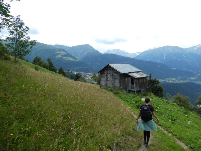 Eine Frau wandert auf dem Aletsch Panoramaweg auf eine kleine Holzhütte zu.