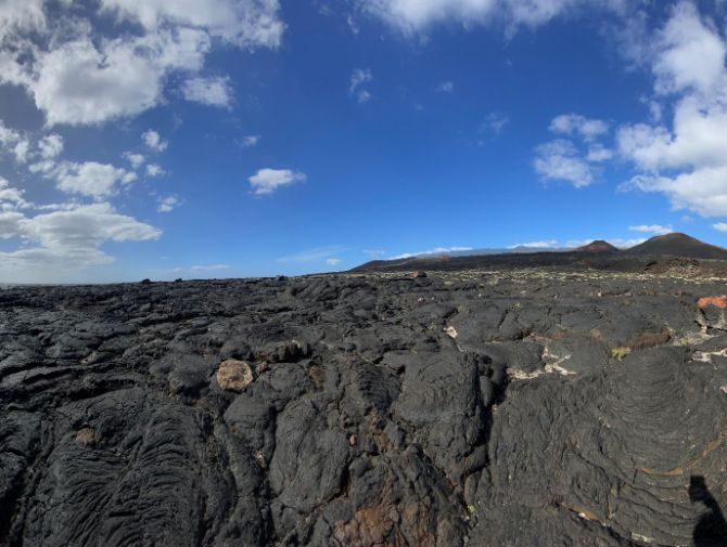 Neben der Küste sieht man Felder voller Lava und den Vulkan im Hintergrund. 