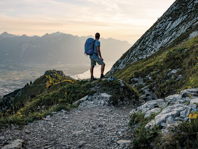 Un randonneur seul avec son sac à dos regarde la vallée depuis la montagne.