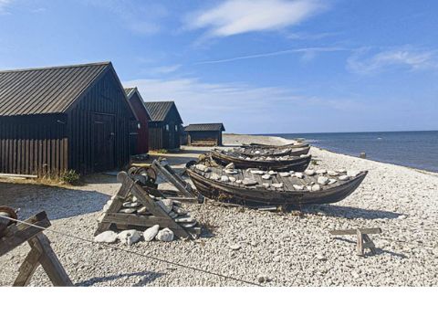 Mehrere Holzhäuser mit Holzbooten vornedran stehen am Strand.