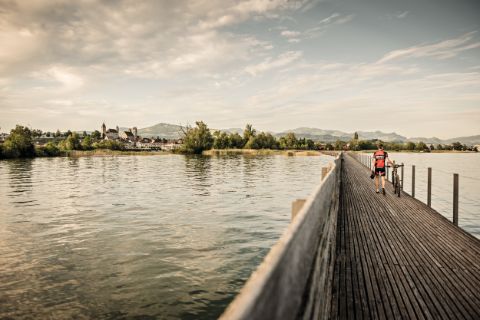 Ein Mann überquert eine Holzbrücke, die in die Altstadt von Rapperswil führt. Herzroute. Veloferien mit Eurotrek.