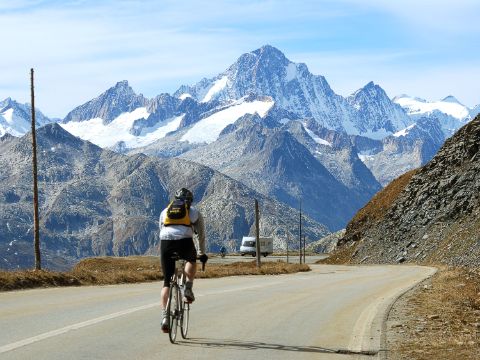 A racing cyclist on a normal road with a view of the Alpine panorama of the Furka Pass.
