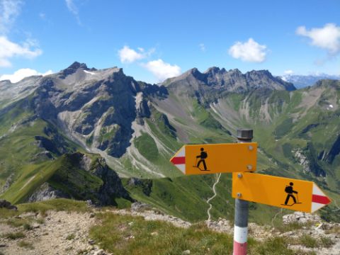 Un panneau indicateur de randonnée se trouve devant un décor de montagnes verdoyantes au Liechtenstein.