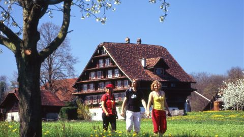 Drei Personen und im Hintergrund ein altes Holzhaus. Alpenpanorama-Weg. Wanderferien mit Eurotrek.