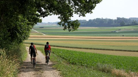 Deux cyclistes sur les chemins rouges entre la lisière de la forêt et les champs.
