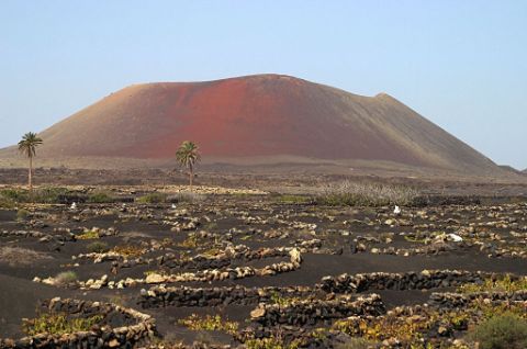 Vulkan in karger Landschaft mit schwarzem Sand umgeben