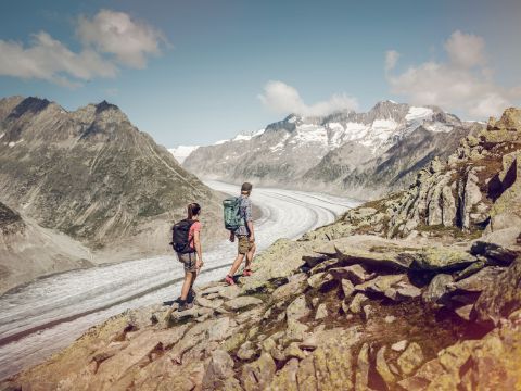 Two hikers walk close to the Aletsch Glacier on a stony path.