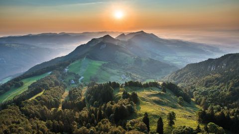 Breathtaking sunrise on the Weissenstein that colours the Hommel on the horizon in a soft orange and turns the mountain and the hills into different shades of green