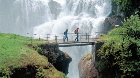Two people on a bridge and a large waterfall in the background. Via Suvorov. Hiking holidays with Eurotrek.