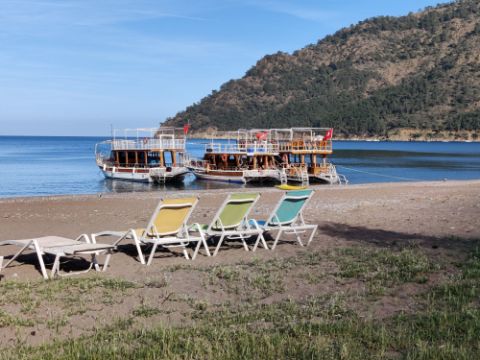 Drei Liegestühle stehen am Strand und im Meer befinden sich drei Holzboote 