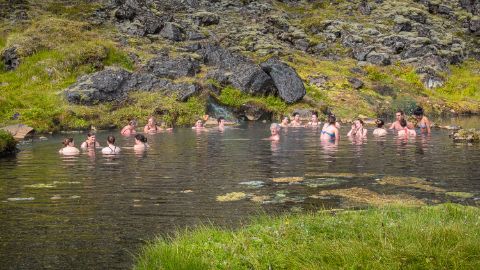 Personen die im Wasser baden, dahinter gleich ein begrünter Hügel