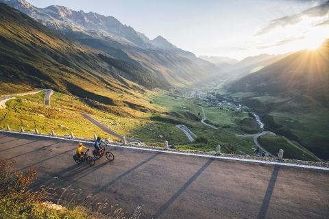 Zwei Velofahrer fahren eine Passstrasse hoch. Im Hintergrund die Bergwelt Graubündens.